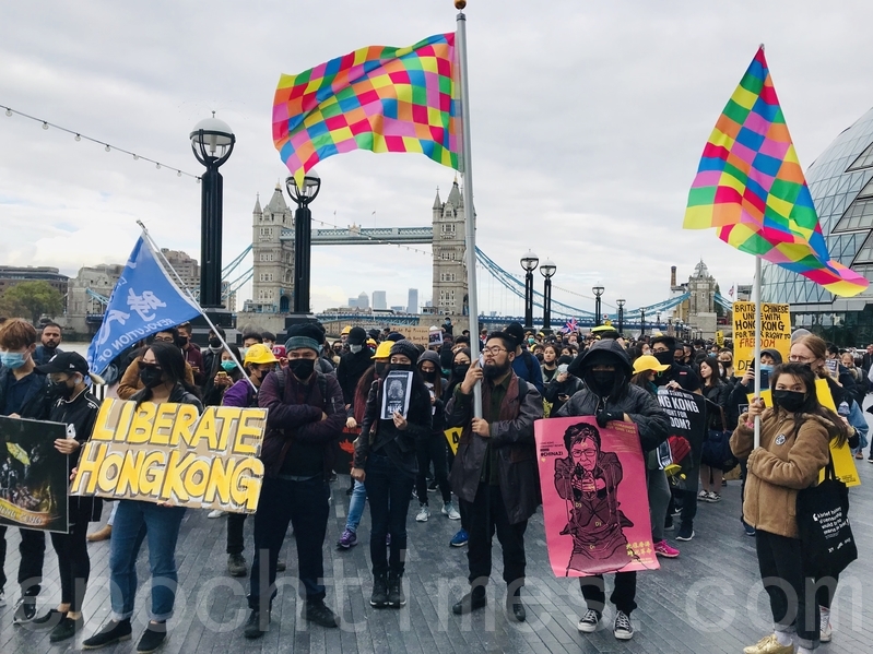 周六（10月5日），巴丟草手持「連儂旗」在遊行隊伍前列，帶頭在英國著名地標倫敦塔穚（Tower Bridge）旁的市政廳出發，沿著泰晤士河南岸（South Bank）河邊遊行抗議。（唐詩韻／大紀元）