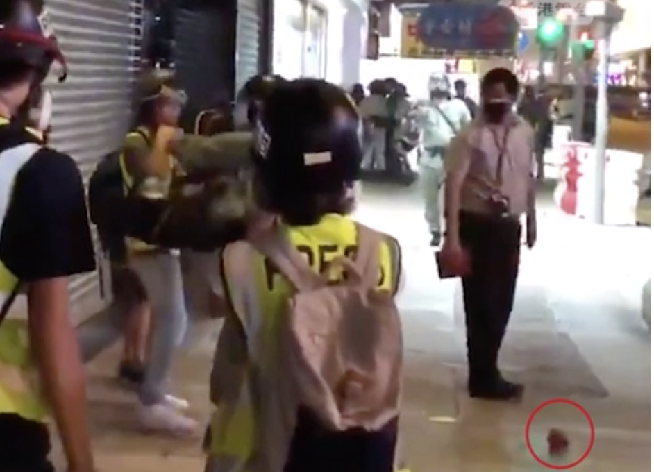 27日晚於旺角，港台記者被防暴警察強行扯下防毒面罩，中共政協律師陳曼琪抹黑記者將手上「磚頭」放落地下，磚塊在地上向前彈開幾呎。（視頻截圖）
