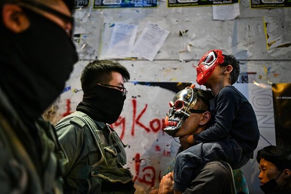 一對戴著面具的父子參加狂歡反送中活動，被警方盤查。（ANTHONY WALLACE/AFP via Getty Images）