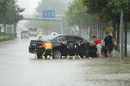 7月20日北京街頭，人們奮力推淪陷在水中的車。（Lintao Zhang/Getty Images）
