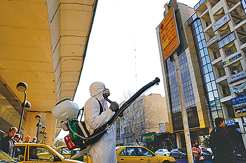 圖為伊朗消防人員和城市工人穿著防護服在首都德黑蘭的一條街道上消毒。(AFP)