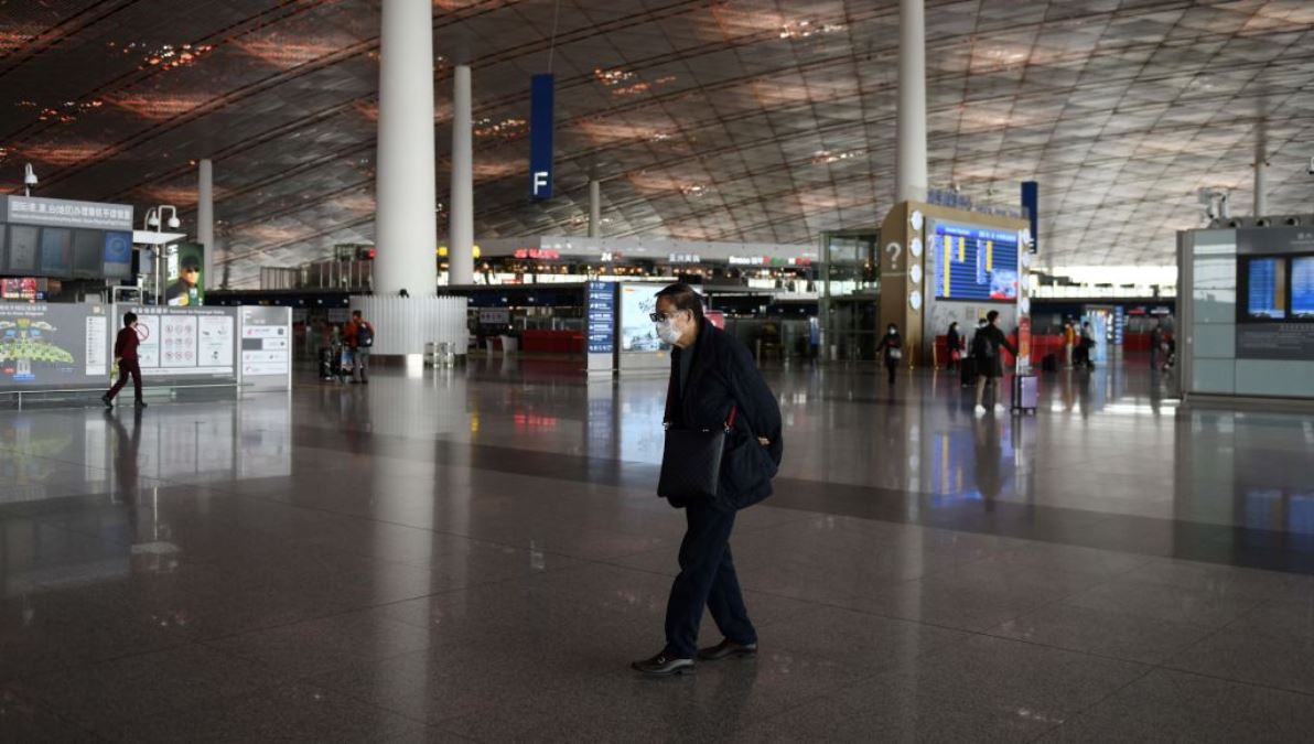 北京首都機場2020年3月11日，一名為預防感染中共肺炎（COVID-19）而戴著口罩的旅客穿過機場空蕩盪的大廳。（GREG BAKER/AFP via Getty Images）
