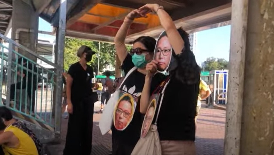 市民舉起印有「快必」照片的頭像面具，並擺出「心」字手勢。（宋碧龍／大紀元）