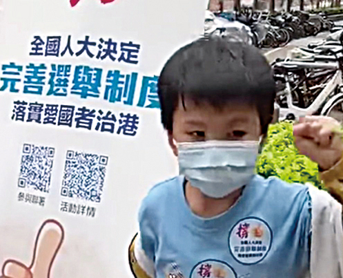 一名5-6歲兒童站在「撐人大決定完善選舉制度」的易拉架前，揮動拳頭，表示「國家要藍 不可以做黃」「黃的不是好人」。（影片截圖）