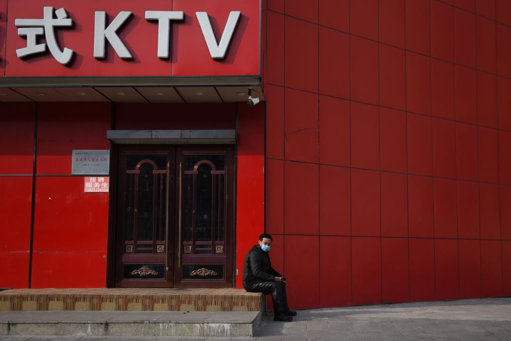 2020 年 2 月 25 日，一名男子坐在北京一間因疫情臨時關閉的卡拉OK廳門外。（GREG BAKER/AFP via Getty Images）