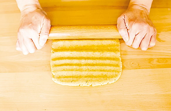 將麵團放在枱面上，塑形成方形後，用擀麵棒由上而下地按壓。