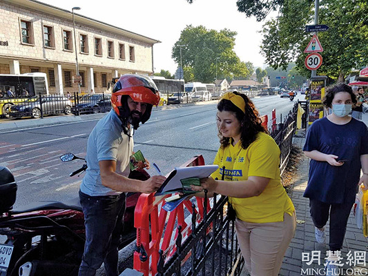 一位騎電單車的男士停下來，在要求解體中共的請願信上簽字。（明慧網）