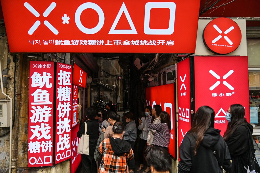 奈飛的韓劇《魷魚遊戲》在全球大火之際，中國也超越「限韓令」，私下掀起滾滾熱潮，不僅眾多網站盜播，而且還仿造劇中的服飾、道具、食品等產品熱賣。圖為2021年10月12日，顧客正在上海街頭排隊購買《魷魚遊戲》裡的同款糖餅。 (HECTOR RETAMAL/AFP via Getty Images)
