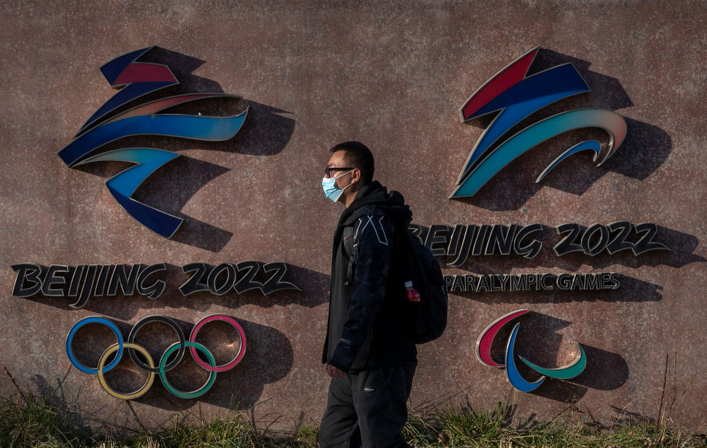 2021年12月7日，一名戴口罩的男子從北京2022年冬奧會和殘奧會的標示前走過，這裡曾是北京首都鋼鐵廠的一座前發電廠，現為北京奧運會組委會總部所在地。（Kevin Frayer/Getty Images）
