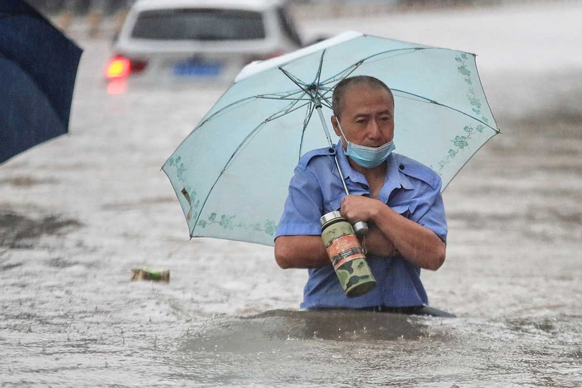 2021年7月20日，受颱風查帕卡影響，河南省鄭州市連日大雨導致街道嚴重水浸，民眾涉水而行。（STR/AFP via Getty Images）