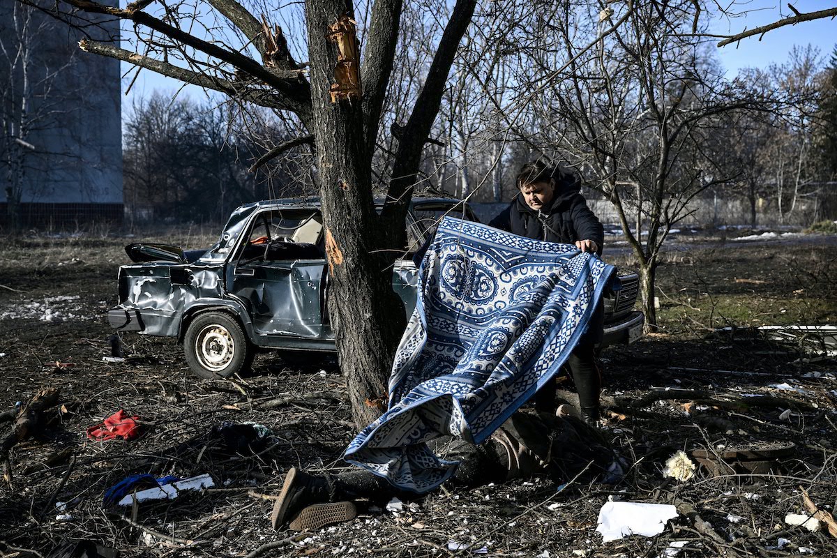 2022年2月24日，烏克蘭東部城鎮丘古耶夫（Chuguiv）發生爆炸事件後，一名男子用地毯蓋住一具躺在地上的屍體。（Aris Messinis / AFP）