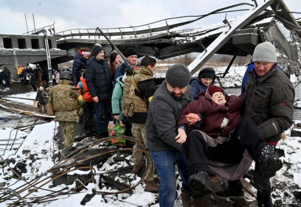 2022年3月8日，烏克蘭士兵幫助一名老年婦女在撤離基輔西北部的伊爾平市時穿過一座被毀壞的橋樑。（SERGEI SUPINSKY/AFP via Getty Images）