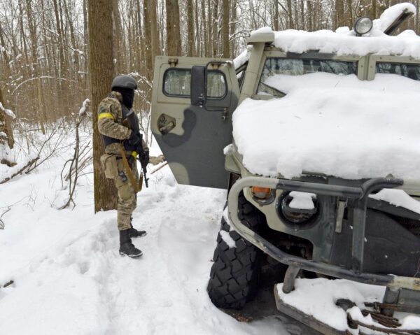 2022年3月7日，在烏克蘭第二大城市哈爾科夫郊外的森林裏，一名烏克蘭國土防禦部隊成員看著一輛被摧毀的俄羅斯軍車。（SERGEY BOBOK/AFP via Getty Images）