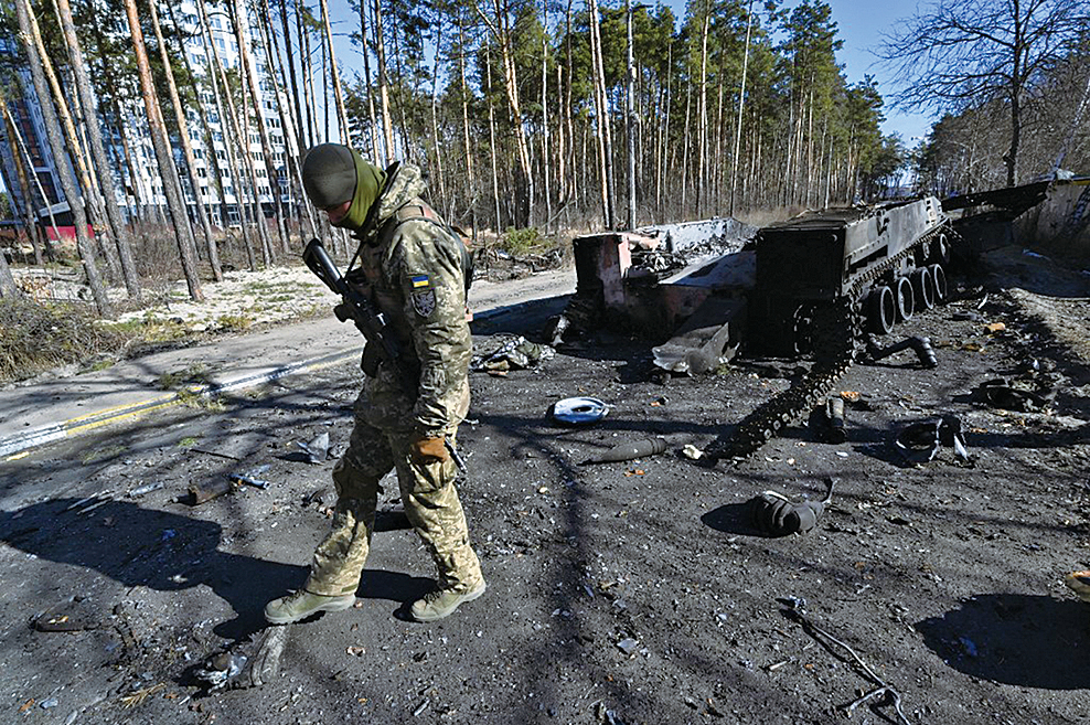 2022年3月12日，一名烏克蘭士兵在基輔以北的伊爾平檢查被摧毀的俄羅斯裝甲運兵車（APC）的殘骸。（Sergei SUPINSKY/AFP）
