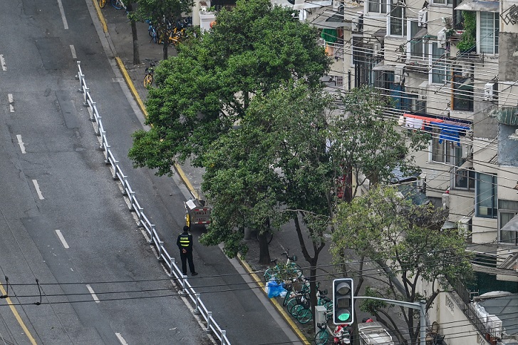 2022年4月20日，上海仍在封城中，一名官員站在靜安區居民樓前的一條街道上。（Hector RETAMAL / AFP）