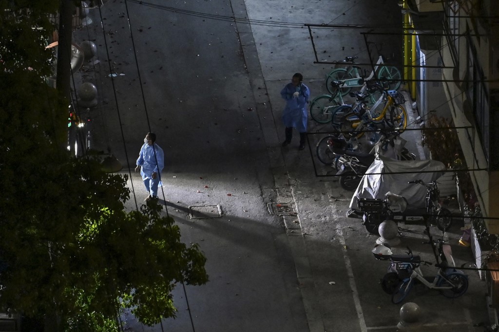 圖為被封鎖的上海靜安區，2022年4月27日晚上，穿著個人防護裝備的工人在街道上走動。 （Hector RETAMAL / AFP）