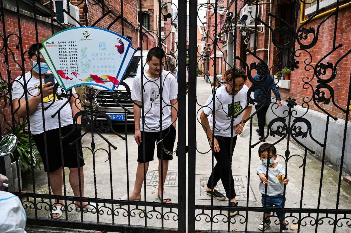 2022年5月30日，在上海靜安區的一個居民區內，居民們站在他們的院子裏。上著鐵鏈子的大門擋住了他們看看外面世界的路。（Hector RETAMAL / AFP）