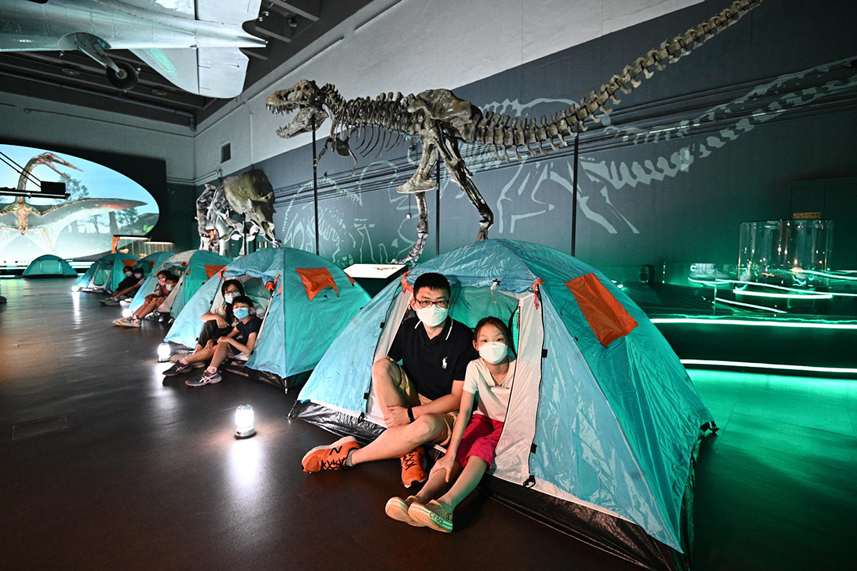 香港科學館8月5日舉行首場「與龍同眠」留宿活動，參加者於展覽廳內恐龍化石下架設的帳篷留宿。（政府新聞處）