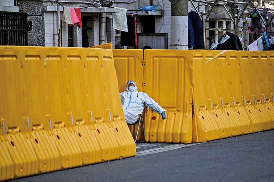 2022年3月29日，在上海靜安區，一名身穿防護裝備的工人在封鎖社區的入口處守衛。（Hector Retamal / AFP）