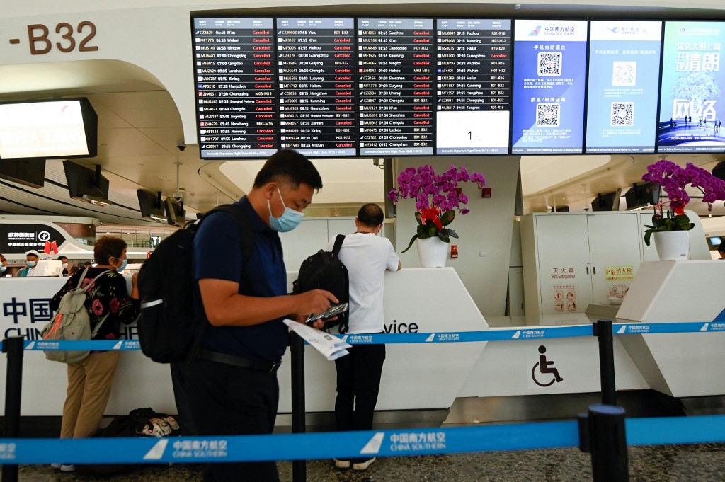 2022年9月21日晚，中國將近六成航班被取消，引發輿論關注。圖為2021年7月12日，在北京大興國際機場候機室，旅客站在顯示取消航班的屏幕前。當時由於暴風大雨，北京數百個航班被取消。（WANG Zhao / AFP）
