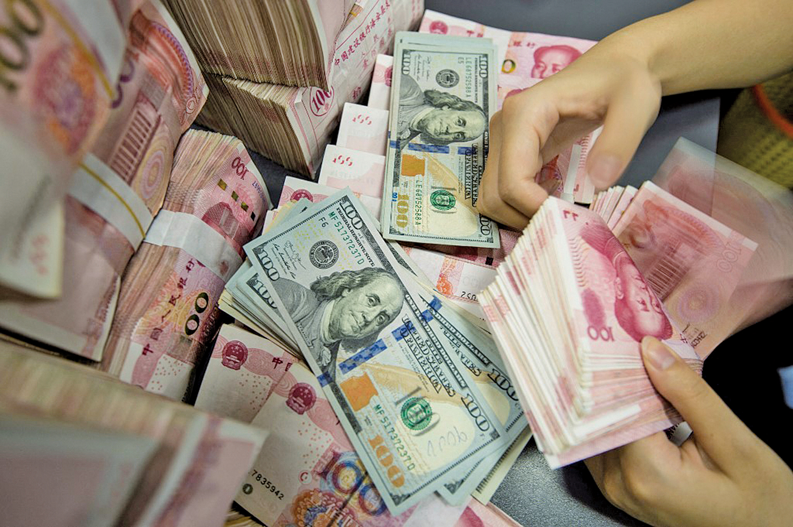 近日，人民幣跌跌不休，離岸人民幣兌美元，已經跌穿了7.14。圖為2019年8月28日，江蘇南通的一家中國銀行內，一名員工在清點人民幣和美元鈔票。(AFP)