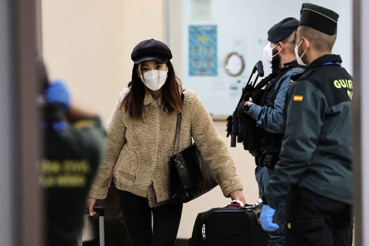 2022年12月31日，一架國航CA907航班降落在西班牙首都馬德里郊區巴拉哈斯的阿道弗·蘇亞雷斯馬德里-巴拉哈斯機場，這是西班牙恢復健康管控後從中國飛來的第一架航班，而此時正是疫情在中國爆發之際。西班牙要求來自該中國的乘客必須接受體溫檢測、出示核酸檢測陰性或證明已接種了西班牙認可的疫苗。圖為一名中國乘客正在從西班牙國民警衛身邊經過。（Pierre-Philippe Marcou / AFP）