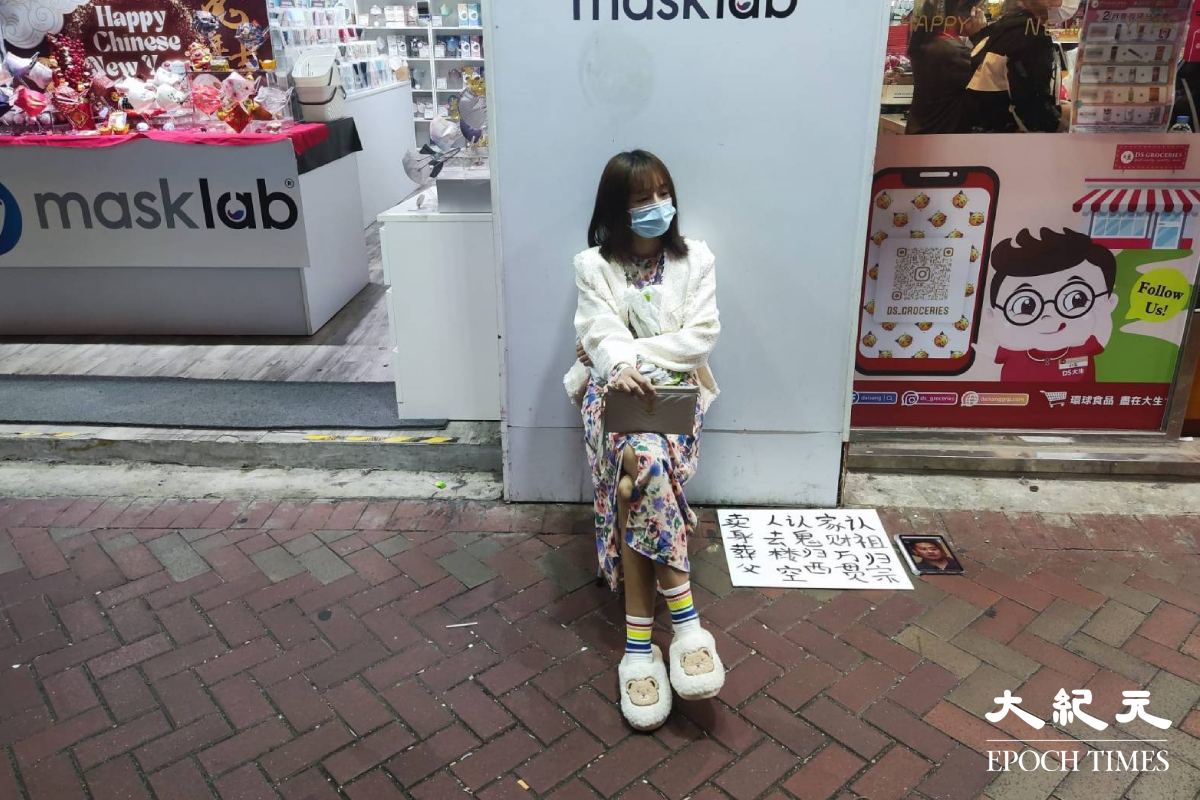 古怪女子坐在旺角亞皆老街近通菜街口，旁邊放有以簡體字寫上的賣身葬父字句。（羅麗莎／大紀元）