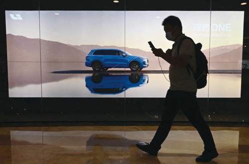 2021年8月12日，北京一家購物中心外，一名男子從宣傳中國某品牌電動汽車的大型廣告牌前走過。資料圖。(JADE GAO/AFP )