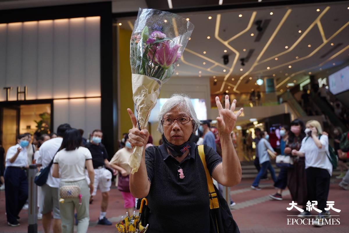 社運人士「王婆婆」王鳳瑤在銅鑼灣記利佐治街手持鮮花，並舉起「五一」手勢，隨後被帶上警車。（劉駿軒／大紀元)