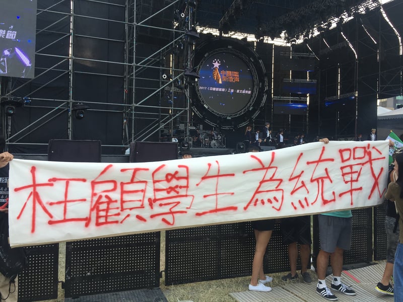 中國大陸選秀節目「中國新歌聲」24日在國立台灣大學舉辦「2017『中國新歌聲』上海・台北音樂節」活動，有民眾到場站在舞台邊，拉開寫上訴求的白布條表達不滿。（中央社）