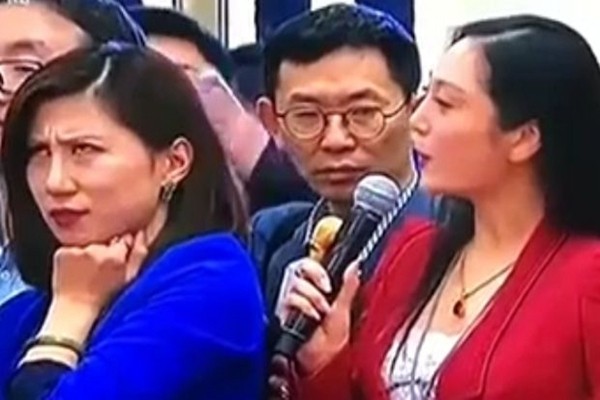 今年3月13日的中共兩會上，紅衣女記者張慧君以美國全美電視（AMTV）執行台長的身份，向中共官員提了一個冗長的問題，且一副官腔，惹得身旁穿藍衣的上海第一財經女記者梁相宜一臉不屑和不耐煩。（視像擷圖）