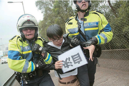 香港眾志秘書長黃之鋒等人昨日趁張德江車隊路經東隧時，手持「自決」的紙張，高叫口號，一度衝出馬路，警員即把他們按在路旁，並將他們拘捕。（香港眾志提供）