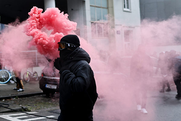 2021年12月5日，比利時布魯塞爾，民眾不滿政府的COVID-19防疫政策，聚集到街上抗議。圖為一位抗議者點燃紅色煙霧彈。（Kenzo Tribouillard/AFP via Getty Images）