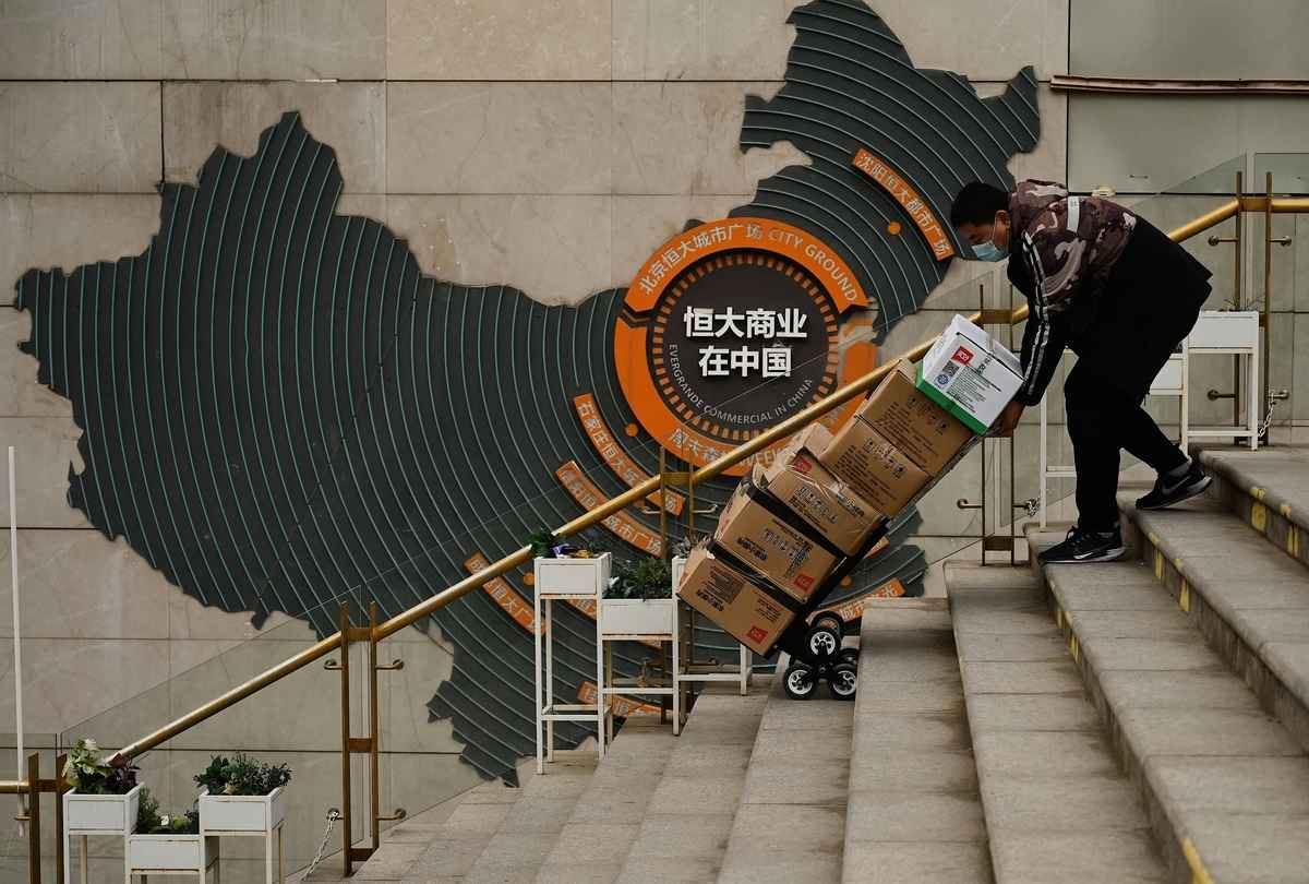 1996年江澤民、曾慶紅當政時，許家印在深圳創辦恒大。許家印攀上曾慶紅家族後，恒大迅速擴張。圖為2021年12月8日，在北京房地產開發商的住宅小區，一名工人在顯示恒大集團中國業務的標誌前推車。（NOEL CELIS/AFP via Getty Images）