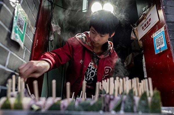圖為2021年4月4日，一個年輕小販在位於北京一個傳統街區的路邊攤位上準備食物。（Nicolas Asfouri/AFP）