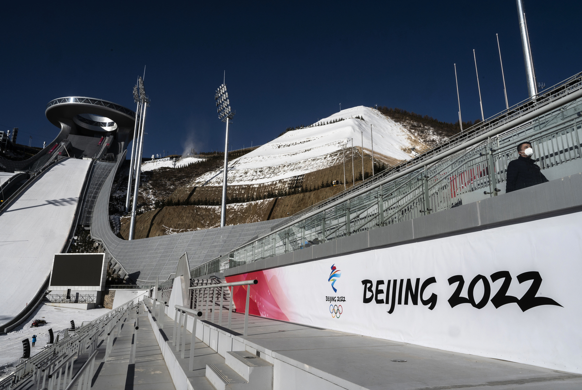 2021年12月21日，在中國北部河北省張家口市崇禮縣，一名工人在國家跳台滑雪中心終點區的標誌旁行走，該中心將在北京2022年冬奧會期間舉辦賽事。該地區將為定於2022年2月4日開幕的北京2022年冬奧會舉辦多項賽事。（Kevin Frayer/Getty Images）
