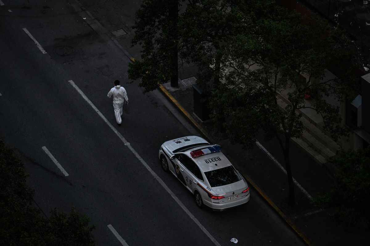 2022年4月11日，上海靜安區COVID-19封鎖期間，一名穿著防護服的工作人員走過街上停著的一輛警車。（Hector Retamal/AFP via Getty Images）