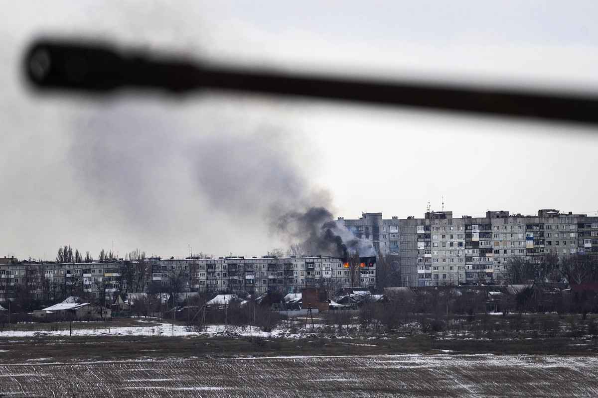 2023年2月14日，在烏克蘭巴赫穆特（Bakhmut），一輛烏克蘭軍車駛過，遠處被俄羅斯炮火擊中的一棟公寓樓正在燃燒。（John Moore/Getty Images）