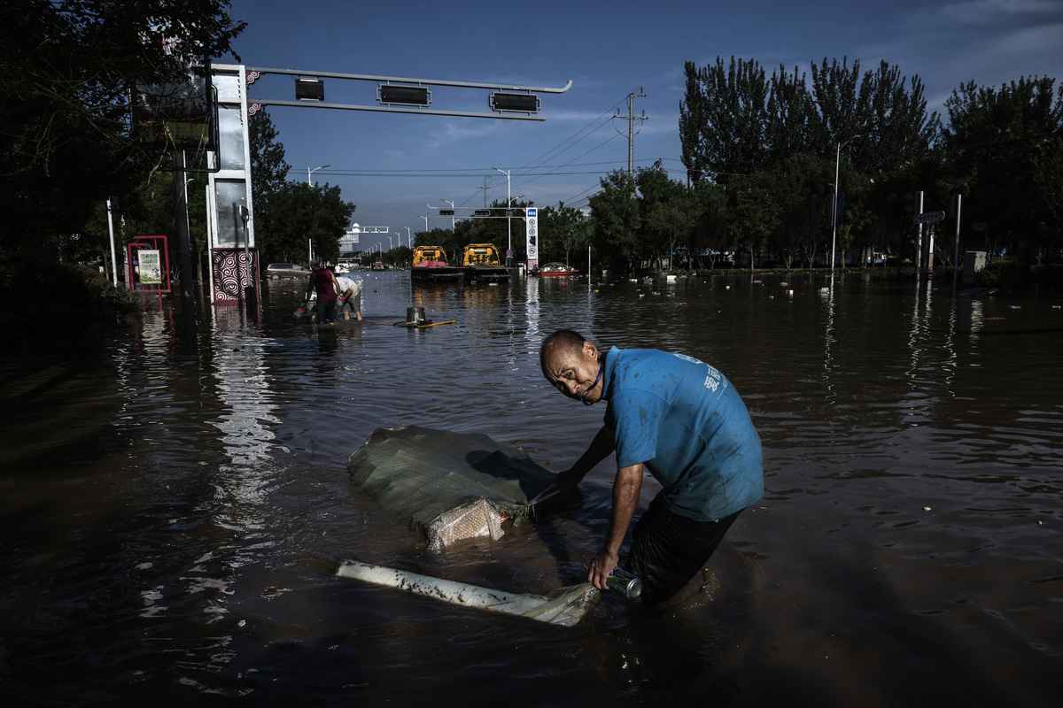 2023年8月5日，河北省涿州市，一名男子蹚過退去的洪水，拉著一個裝滿從建築物中搶救出來的物品的袋子。（Kevin Frayer/Getty Images）