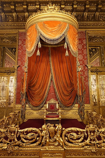 宮殿的王座室被金色和深紅色覆蓋，展示了王宮的奢華。在極度裝飾和多鏡的空間中，寶座本身在天篷下看起來很小。設計複雜的金色圍欄將國王的座位與那些站在他面前的人隔開。（Guilhem Vellut/CC BY 2.0）