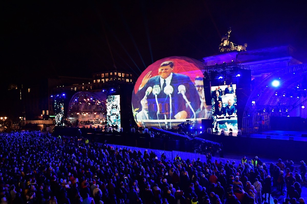11月9日晚，十萬多觀眾參加了柏林市中心地標勃蘭登堡們前的慶祝活動，把紀念柏林圍牆倒塌30周年系列慶典推向高潮。圖為晚會上柏林國立樂團在巴倫博伊姆（Daniel Barenboim）的指揮下演奏了貝多芬名曲《命運交響曲》。大型屏幕上打出了當年美國總統甘迺迪在西柏林演講的畫面，他的名句「我是柏林人」鼓舞著當時被柏林圍牆圍困的柏林人堅持自由民主價值。（TOBIAS SCHWARZ/AFP/Getty Images）