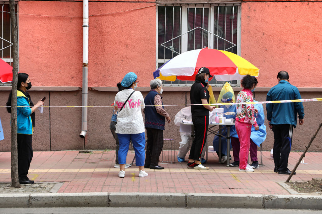 11月12日，黑龍江一店員午睡未戴口罩被黃牌警告。圖為黑龍江牡丹江市的一條街道上，人們戴著口罩排隊等待接受核酸檢測。（STR/AFP via Getty Images）