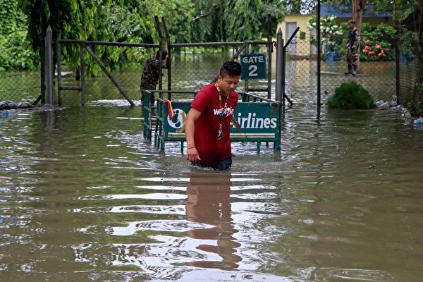 2021年10月20日,尼泊爾比拉德訥格爾(Biratnagar),豪雨成災,一名航空公司員工拉著一輛手推車涉水通行。(LILA BALLAV GHIMIRE/AFP via Getty Images)