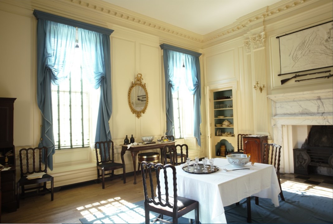 一樓餐廳安排社交活動和其它商務。喬治‧華盛頓(George Washington )是餐廳的常客。木鑲板、簷口線板、壁柱,以及扁平的柱子都漆上中性牛油色。窗簾挑選柔和藍色調,讓觸及天花板的大型窗戶,多份優雅情懷。壁爐三面方框和壁爐上緣層架,採用細緻的藕荷色(藍加灰色)的意大利大理石製成。角落的內嵌式層板餐櫃展示餐廳所需物品。(J.H. Smith/Cartio提供)