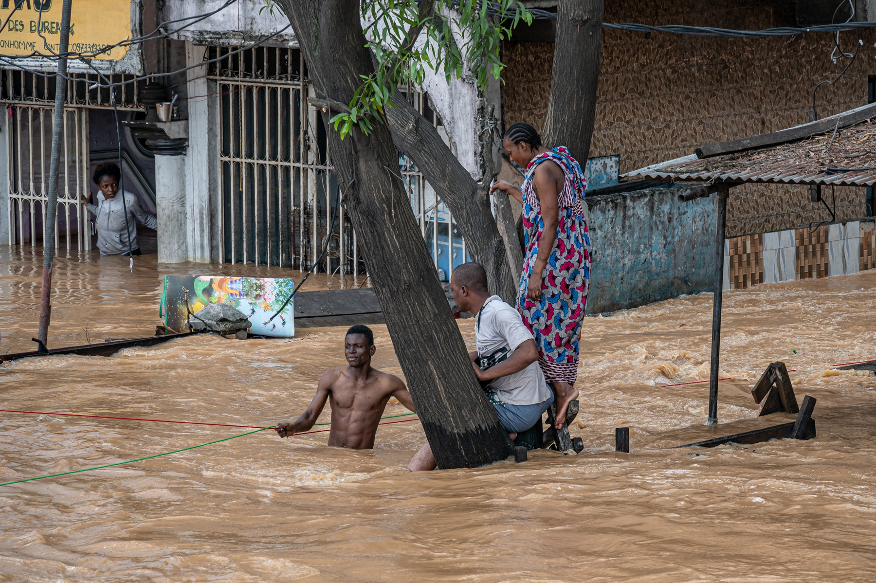 2025年4月6日,民主剛果首都金沙薩恩吉利區(Ndjili district)遭到暴雨襲擊,一條道路被洪水淹沒,居民站在一棵樹上避險。(Hardy Bope/AFP via Getty Images)
