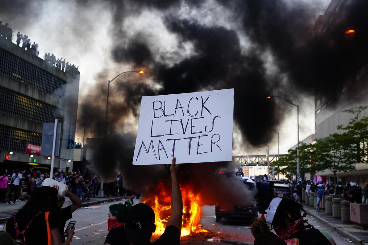 2020年5月29日,在亞特蘭大CNN中心外,一名男子手持「黑人生命至上」(Black Lives Matter)標語,抗議喬治‧弗洛伊德(George Floyd)之死,一輛警車正在他面前燃燒。(Elijah Nouvelage/Getty Images)