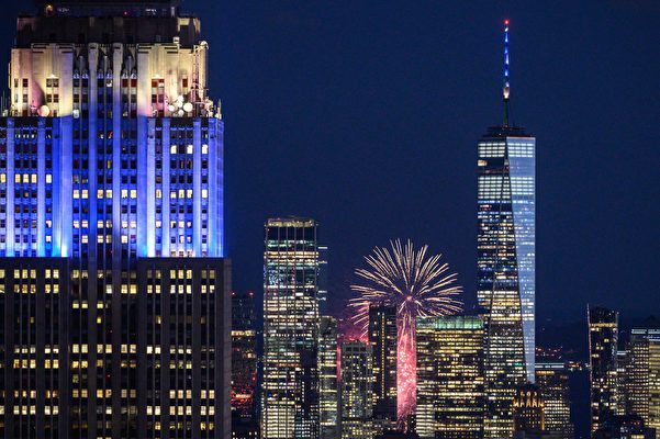 2021年6月15日，煙花在紐約曼哈頓城市天際線的地標性建築後面爆炸，包括帝國大廈（左）和世貿中心一號（右）等建築被染上藍色和金色。這一天，70%的紐約成年人接受第一劑中共病毒（武漢肺炎、COVID-19）疫苗。 （ED JONES/AFP via Getty Images）