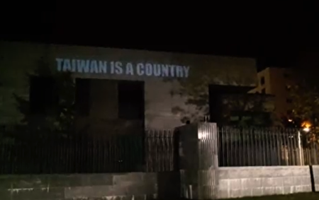 2021年10月3日晚，五毛新聞網（Wumao.news）成員在慕尼黑中共領事館外面，用投影儀將畫面投放在中領館大樓和牆上。圖為「台灣是個國家」。（Hadrian Schattner提供）