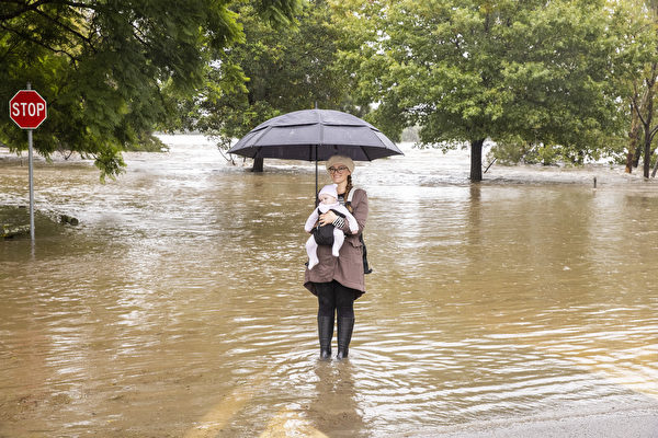 2021年3月21日，澳洲悉尼，霍克伯里河（Hawkesbury River）氾濫成災，一位市民抱著嬰兒涉水通行。（Jenny Evans/Getty Images）