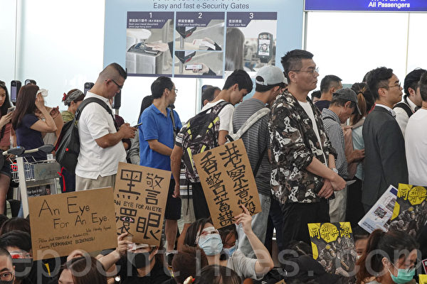 2019年8月12日，港人在香港機場展開「警察還眼」集會。圖為示威民眾舉著「香港警察蓄意謀殺」、黑警」、「還眼」等各式標語表達抗議。（余鋼／大紀元）